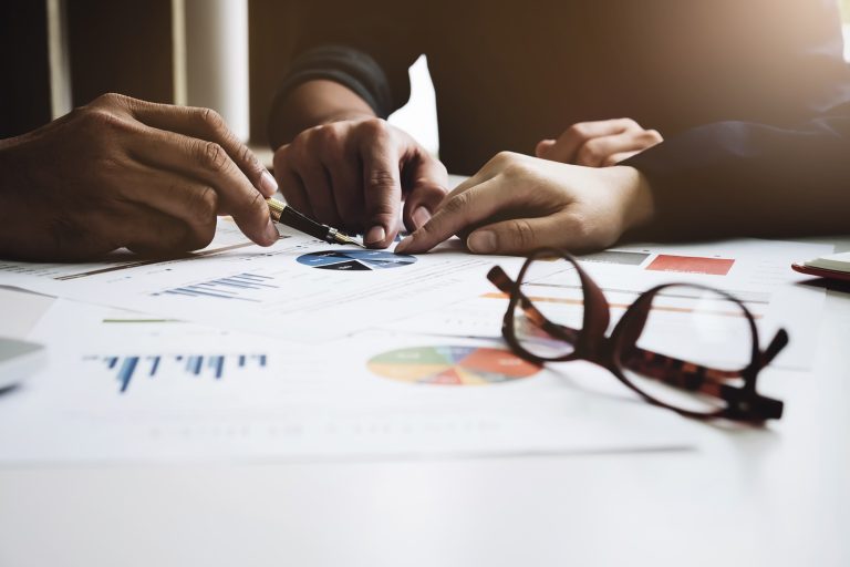 Young businessmen holding a pen and partnership  pointing the graph to analyze the marketing plan on wood desk in office